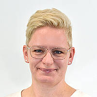 Eine junge Frau mit Brille und kurzen dunkelblonden nach hinten gekämmten Haaren lächelt.