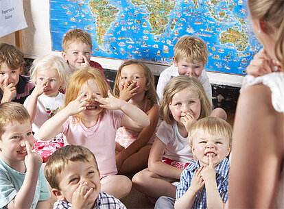 Eine Kita-Gruppe von Kindern schneidet Grimassen mit Fingern vorm Gesicht. 